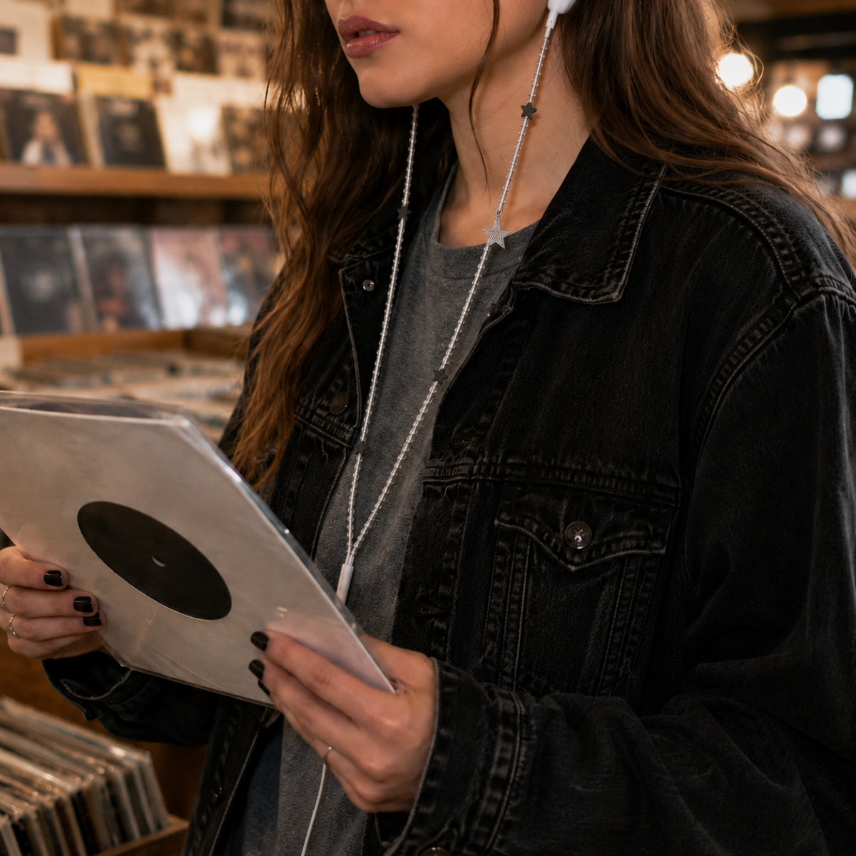 Silver star earphones trailing from a black denim jacket pocket while browsing vinyl records in an indie record store