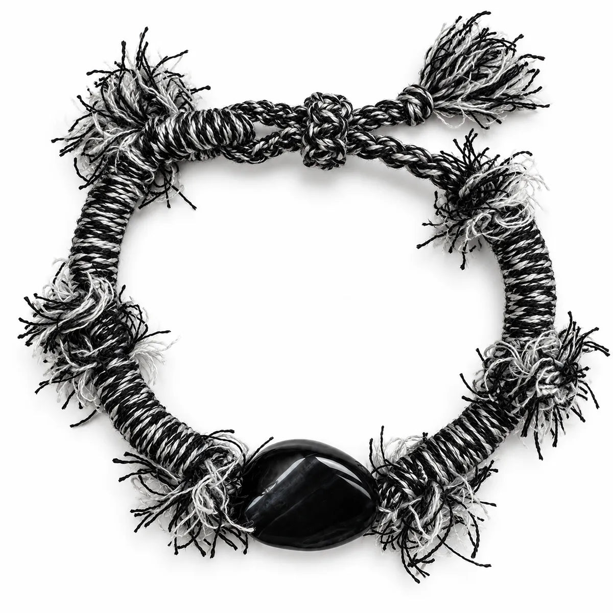 Black obsidian bracelet with a polished black stone on black-and-white wrapped cord with frayed fringe tufts