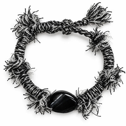 Black obsidian bracelet with a polished black stone on black-and-white wrapped cord with frayed fringe tufts