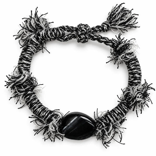 Black obsidian bracelet with a polished black stone on black-and-white wrapped cord with frayed fringe tufts