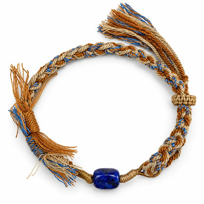 Lapis lazuli bracelet with a deep blue stone flecked with gold pyrite on camel, sand, and blue braided cord with tassels