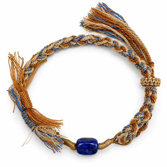Lapis lazuli bracelet with a deep blue stone flecked with gold pyrite on camel, sand, and blue braided cord with tassels