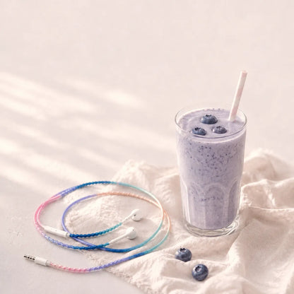  Soft pink and blue milky gradient wrapped earphones coiled beside a glass of blueberry milkshake with fresh blueberries and pale linen napkin in a dreamy blueberry milk aesthetic ad 