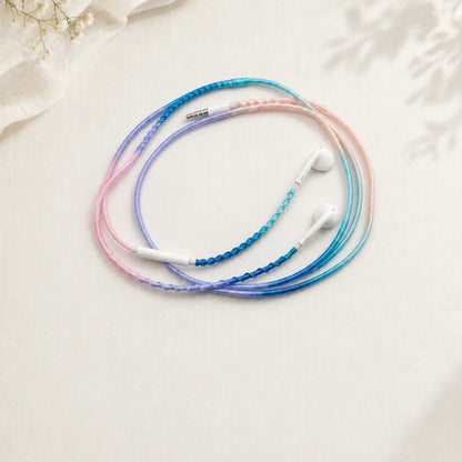  Soft pink and blue milky gradient wrapped earphones coiled into a perfect circle on creamy off-white textured surface for dreamy pastel gradient product ad 