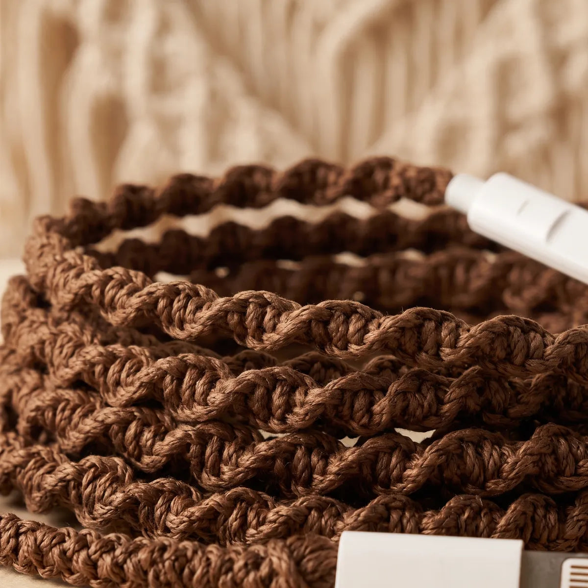  Macro close-up of natural brown macrame open-knot wrapped earphone cord with a real macrame wall hanging in soft focus behind it for boho cottagecore craft aesthetic ad 