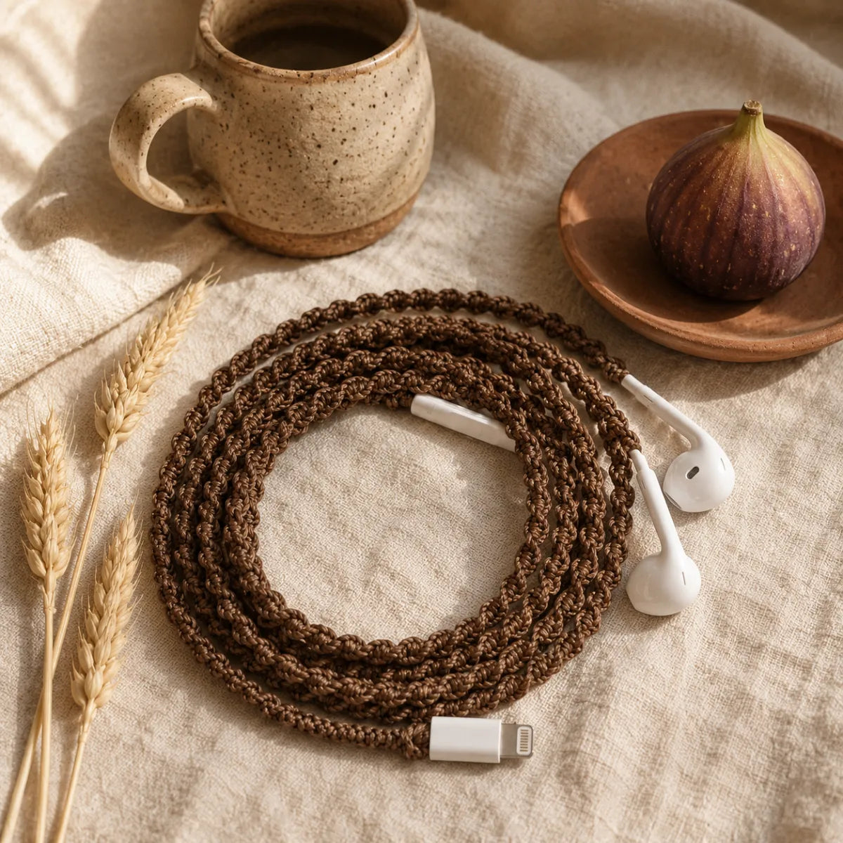  Natural brown macrame open-knot wrapped earphones arranged on natural linen with a handmade ceramic mug, terracotta dish, and dried wheat stalks in a boho still life ad 
