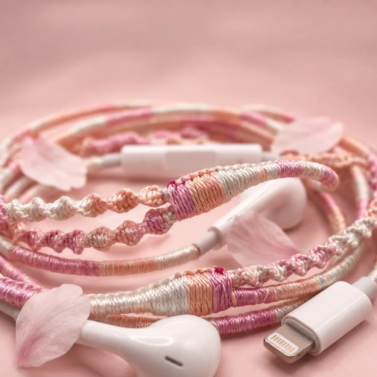  Extreme close-up macro of soft pink peach and cream segmented wrapped earphone cord with scattered cherry blossom petals on a soft blush mist background coquette aesthetic 