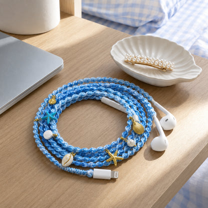  Blue braided shell charm earphones coiled on a dorm desk beside a shell trinket dish and pearl hair clip in morning light 