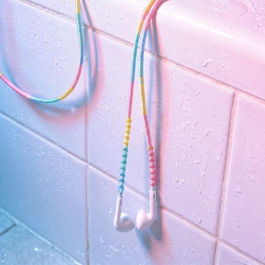  Cotton candy four-color block wrapped earphones draped over a white tile bathtub edge with a smartphone playing music in cool blue Y2K wet-look bathroom aesthetic 