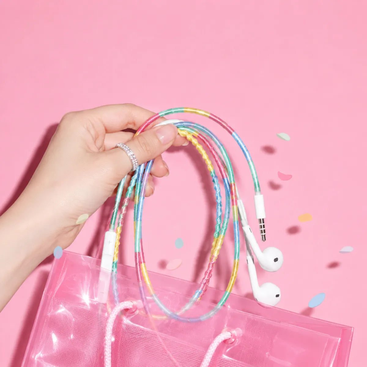  Young hand pulling pastel four-color block wrapped earphones out of a translucent pink shopping bag with confetti for a cute TikTok haul aesthetic ad 