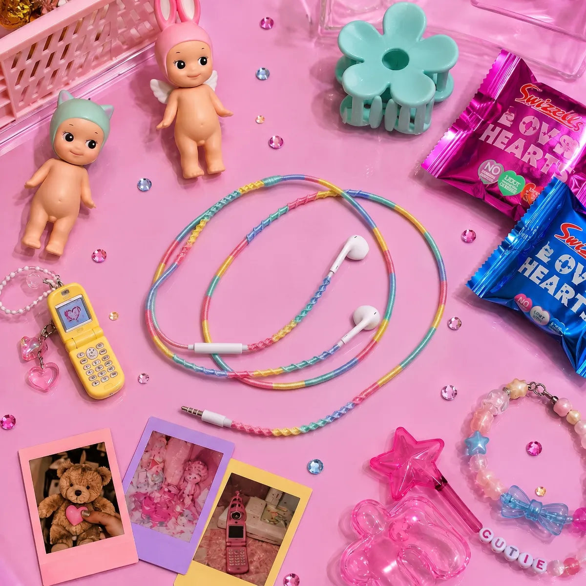  Bright pastel acrylic desk top-down flat lay with cotton candy four-color block earphones coiled around Sonny Angel figurines, pastel claw clip, candy wrappers, and Polaroid snaps 