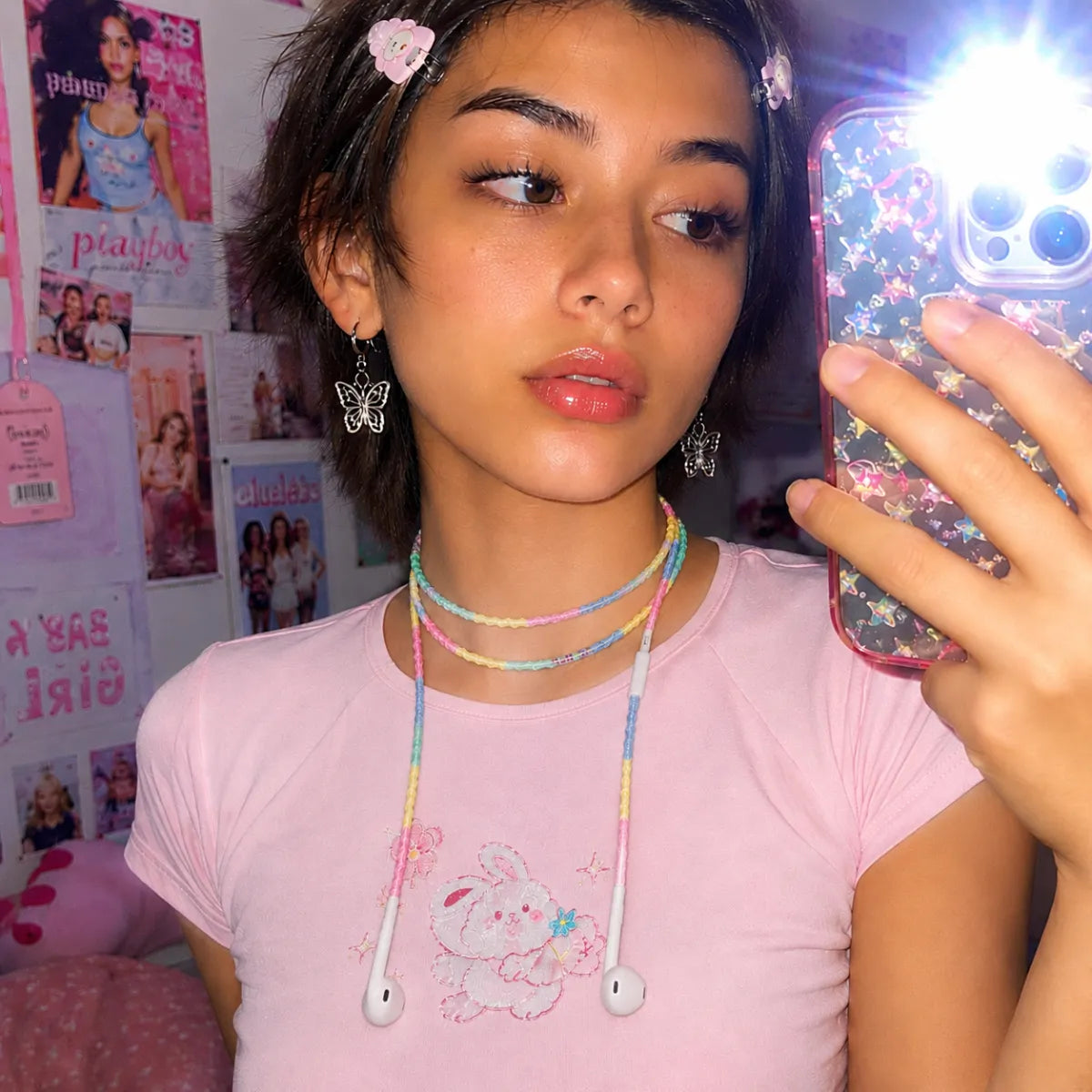  Y2K mirror selfie with hard flash showing young Gen Z girl in pastel baby tee and silver butterfly earrings wearing cotton candy four-color block earphones as a colorful necklace 