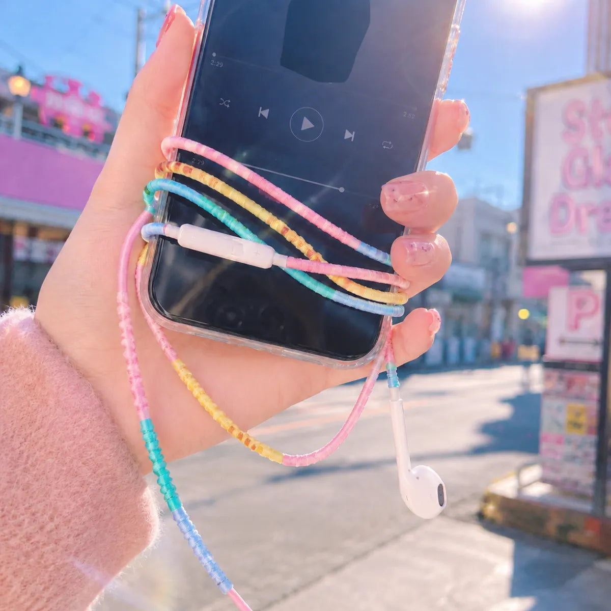  First person POV of hand plugging cotton candy four-color block earphones into smartphone in direct sunlight with each pastel color block popping vividly 