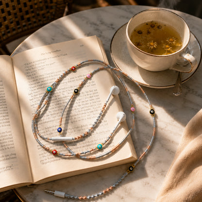 Evil Eye Earphone Wrap placed beside a cup of tea in a cozy café-inspired lifestyle setting.