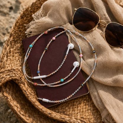Evil Eye Earphone Wrap styled with sunglasses and travel accessories on natural woven textures.