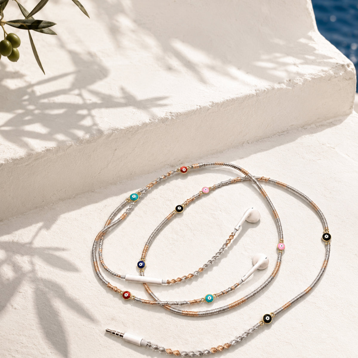 Evil Eye Earphone Wrap with gold and silver braided cord and protective charm accents displayed on a clean white surface.