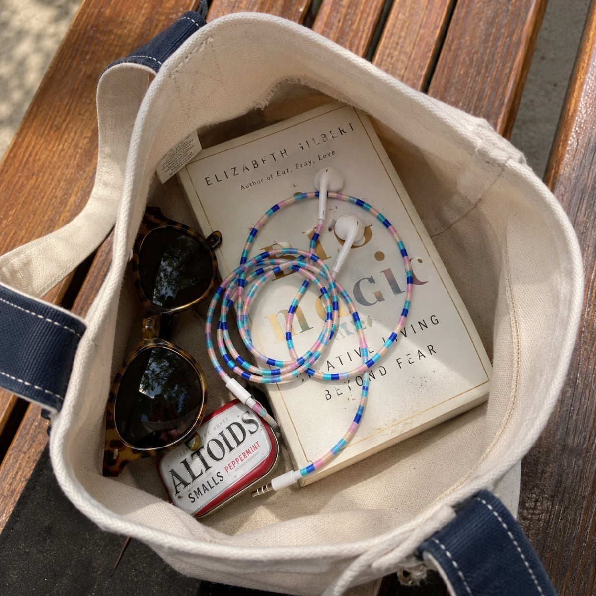 Friendship Bracelet Earphone Wrap resting inside a canvas tote bag with everyday essentials in a casual lifestyle setting.
