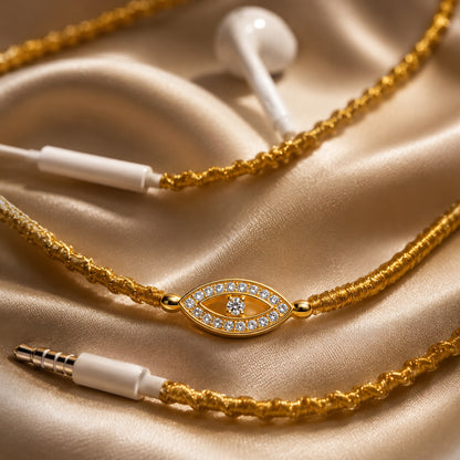  Macro close-up of gold wire-wrapped earphone cord with sparkling evil eye rhinestone charm on cream satin fabric 
