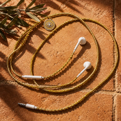  Gold evil-eye-medallion earphones on sun-warmed terracotta tile with soft-focus olive branch under strong Mediterranean sunlight, concept ad 