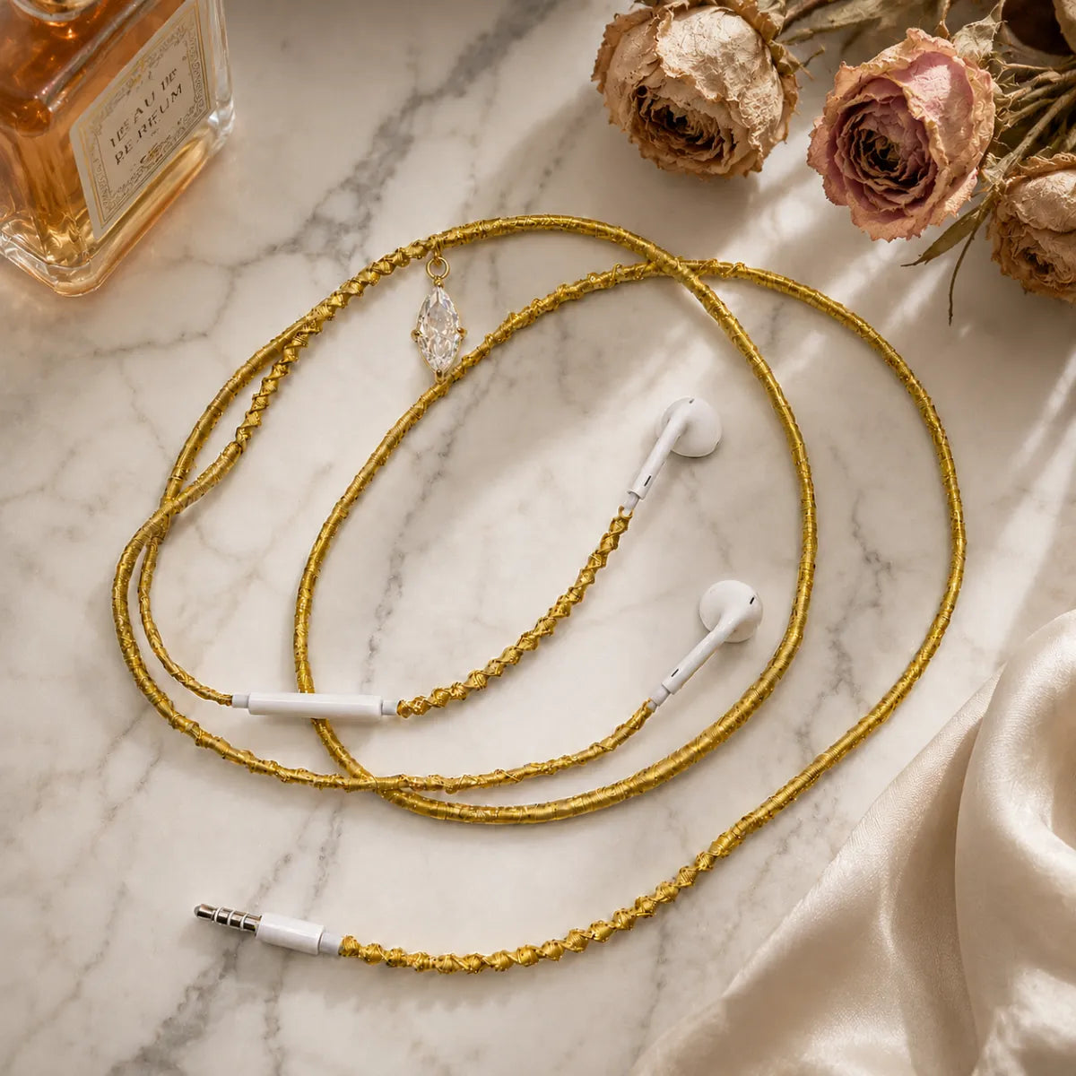 Gold marquise-crystal earphones on white marble vanity with amber perfume bottle, dried cream and dusty-pink roses and ivory silk scarf in soft window light 