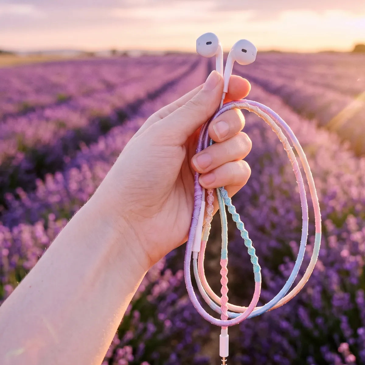  Hand holding lavender dominant pastel gradient wrapped earphones above a real lavender field in golden hour summer evening light fairycore aesthetic 