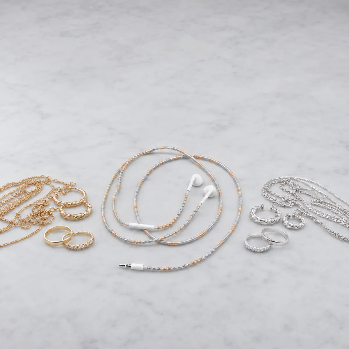  Mixed metal wrapped earphones placed between a pile of gold jewelry and a pile of silver jewelry on neutral grey surface, solving the gold-or-silver dilemma 