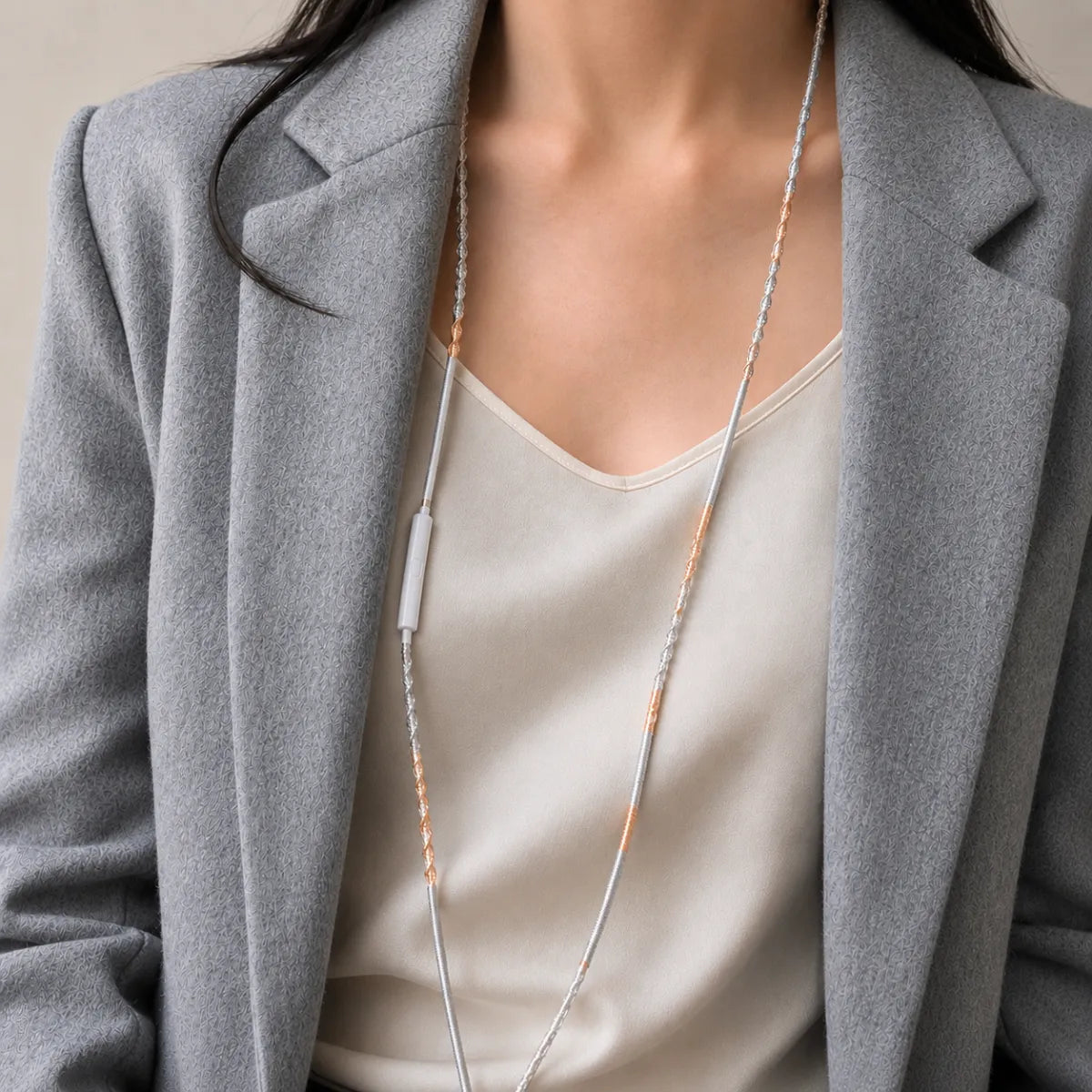 Close detail of neutral minimalist outfit in cream and grey tones with mixed metal wrapped earphone cord visible draped across the chest as a metallic styling accent 
