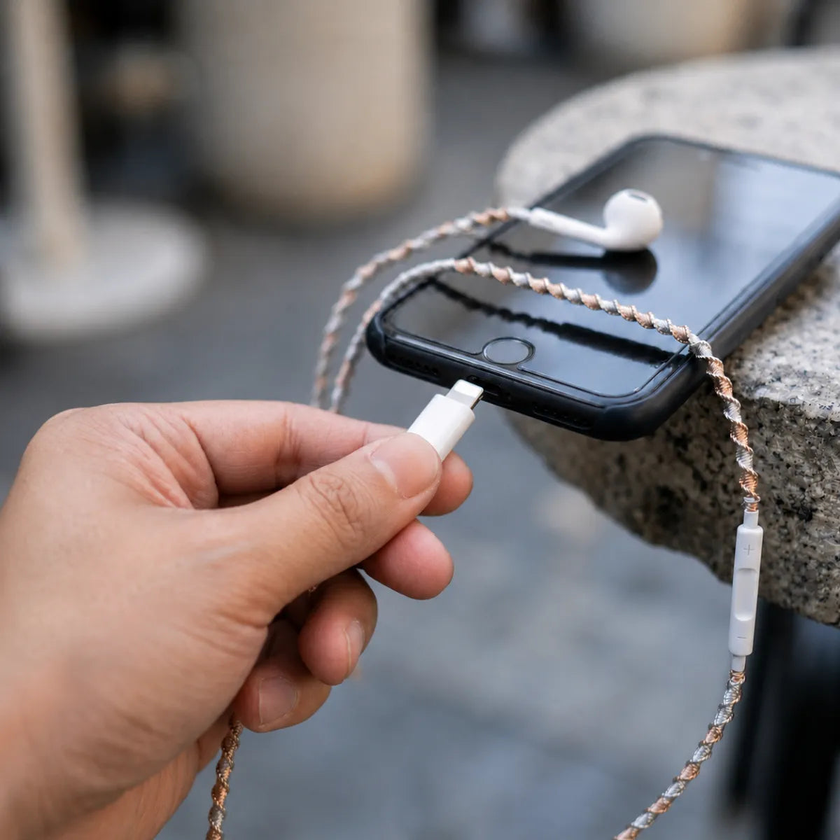  First person POV of hand plugging mixed metal wrapped earphones into smartphone in natural daylight, gold and silver wrap visibly catching the light 