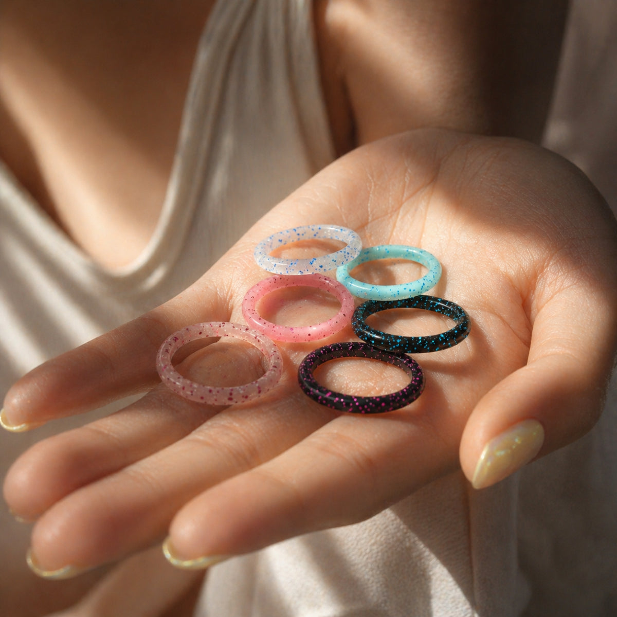 Norelva glitter silicone rings for women in six sparkle colors held in a hand with soft natural light