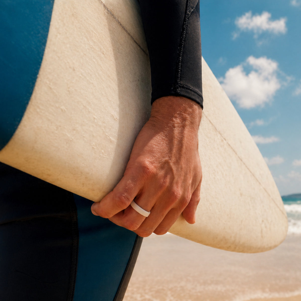 man wearing white silicone ring holding surfboard on beach, safe flexible ring for surfing and active lifestyle