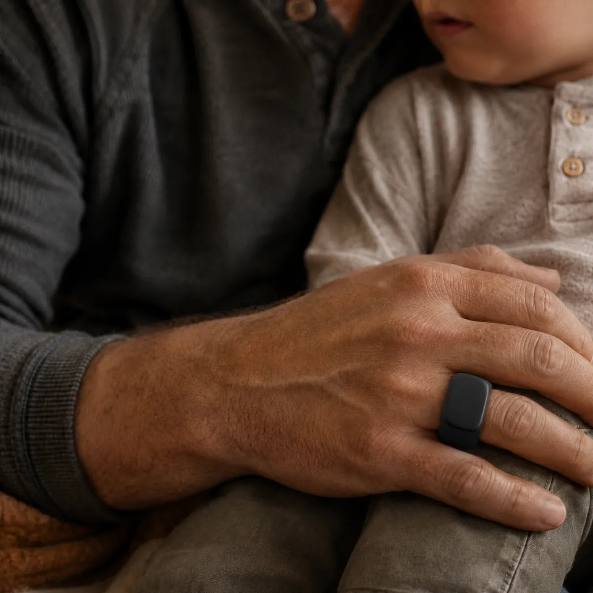 Close-up of a man wearing a black silicone signet ring with a square face, resting his hand on a child’s knee in a warm family moment, highlighting the matte texture and modern design of the ring