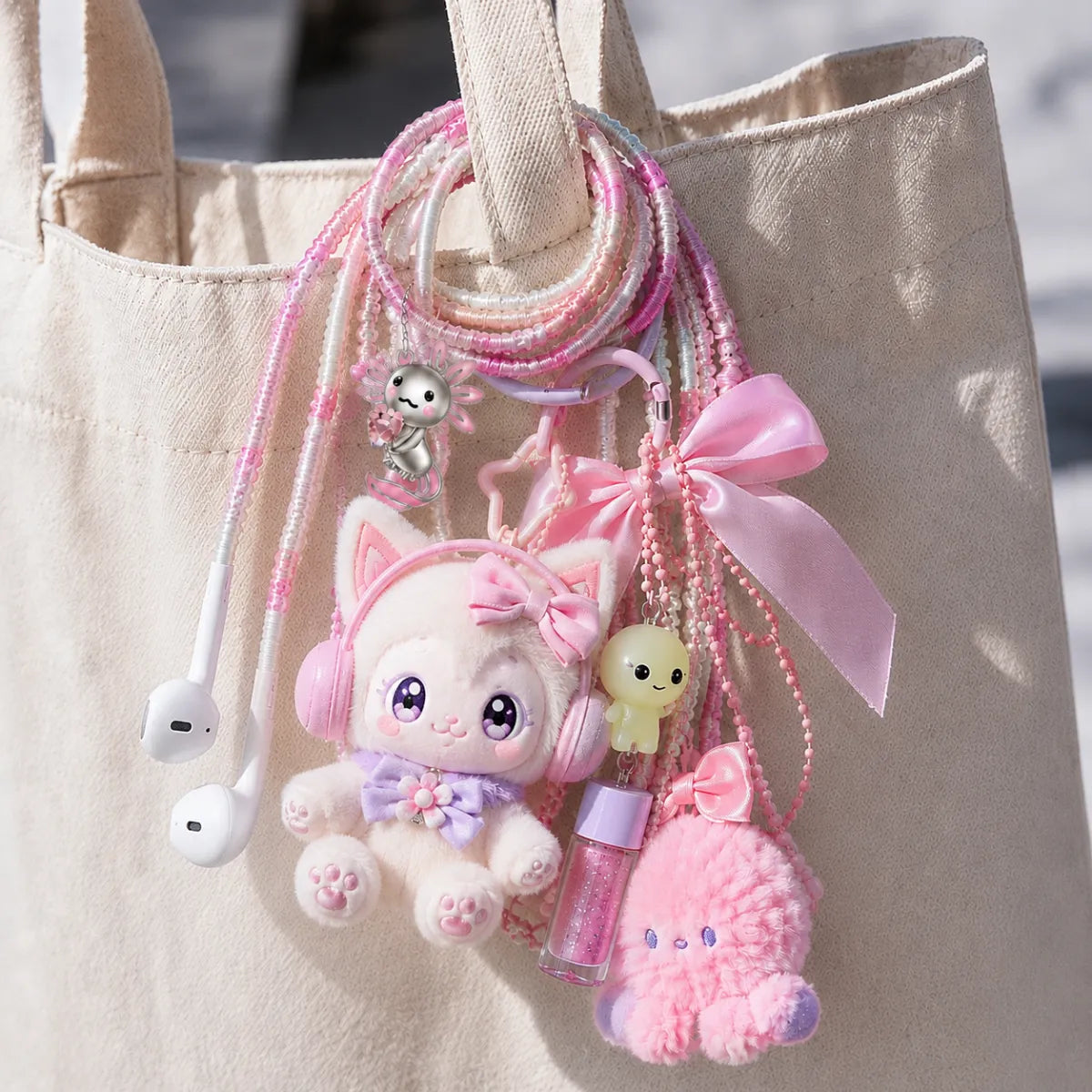  Pink axolotl earphone wrap looped onto a canvas tote strap as a bag charm clustered with Labubu-style plush, lip gloss, and ribbon accessories 