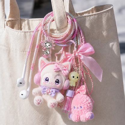  Pink axolotl earphone wrap looped onto a canvas tote strap as a bag charm clustered with Labubu-style plush, lip gloss, and ribbon accessories 