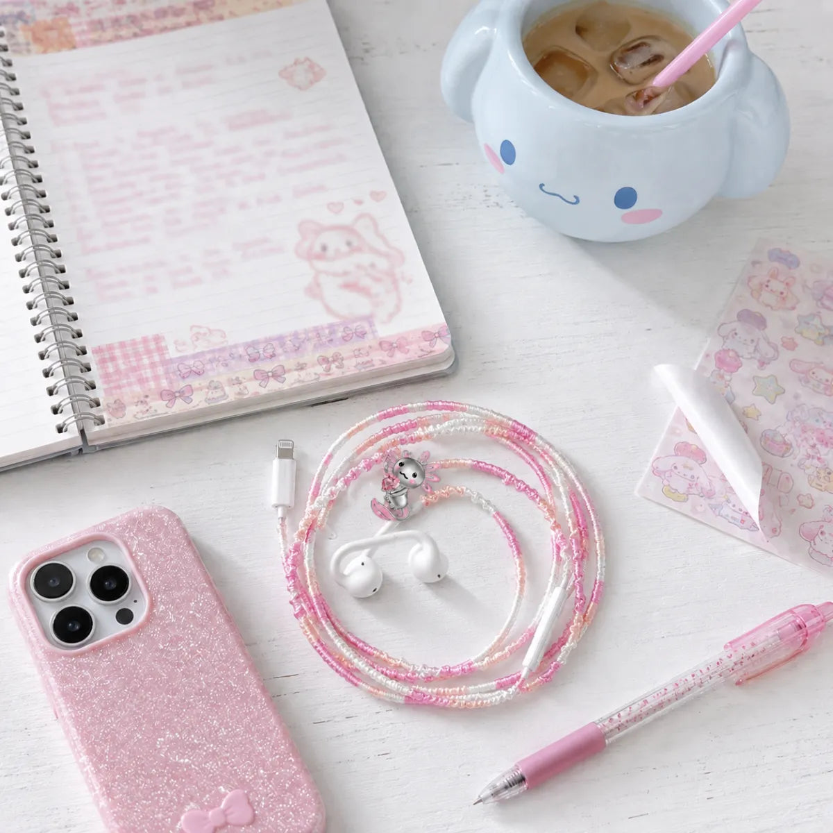 Kawaii pink axolotl earphone wrap on a white desk with washi-tape journal, character-style mug, kawaii stickers, and sparkly pink phone 