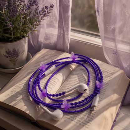  Purple butterfly earphones on an open hardcover novel on a window ledge with sheer purple curtains and a small potted lavender plant in warm afternoon light 