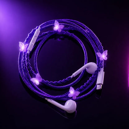  Purple butterfly-charm earphones laid on glossy black surface under violet and magenta gel lighting, high-fashion editorial ad 