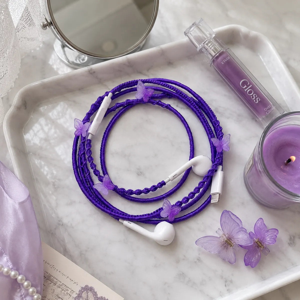  Purple butterfly earphones on white marble vanity tray with purple lip gloss, butterfly hair clips and lavender candle in soft daylight 