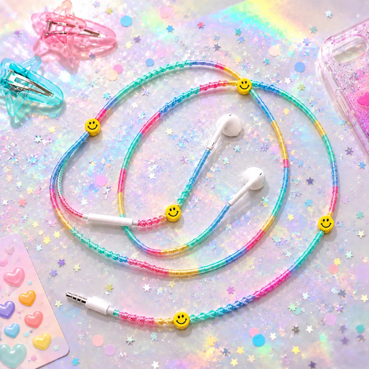  Pastel rainbow smiley-charm earphones spiraled on iridescent surface with pastel confetti, hair clips and phone case, festival flat-lay ad 