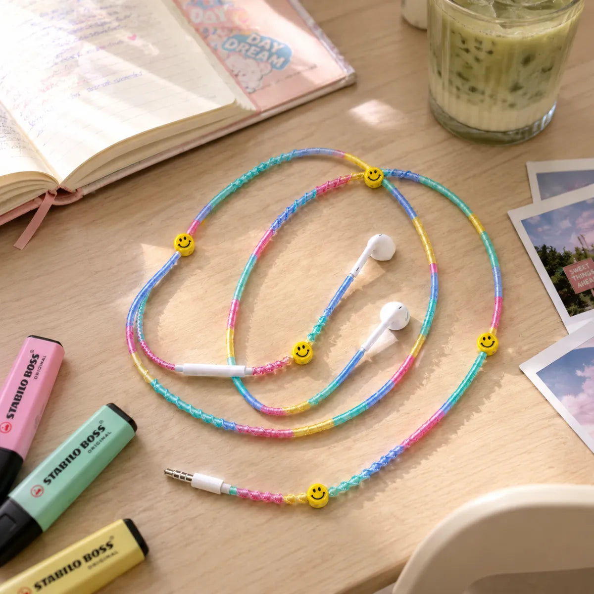  Pastel rainbow smiley earphones on a light-wood study desk with pastel notebook, highlighters and iced matcha latte in soft afternoon light 