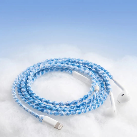  Sky blue crochet wrapped earphones with white Lightning connector resting on a soft white cloud-textured surface against a pale blue sky gradient for a piece of sky aesthetic ad 