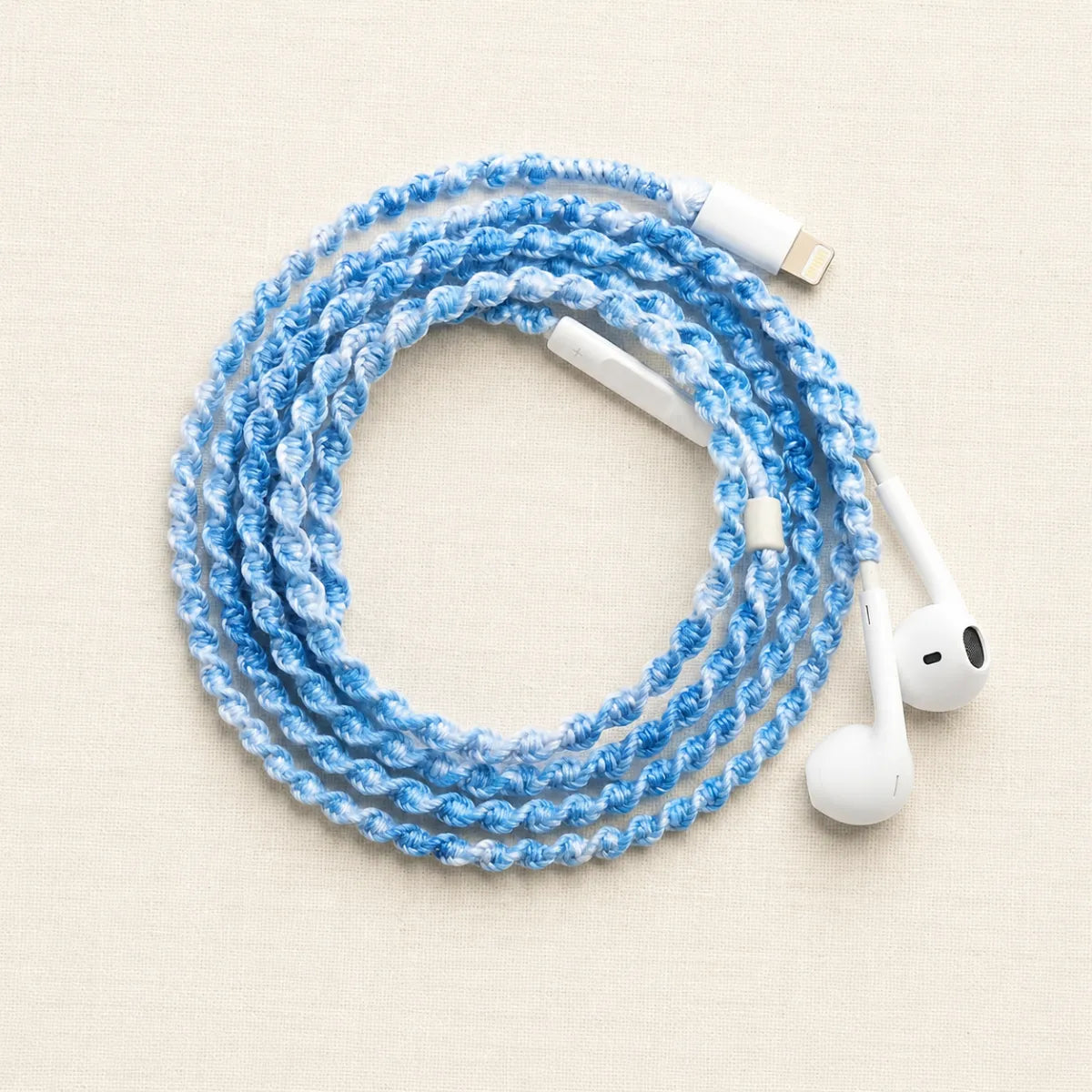  Sky blue crochet wrapped earphones coiled into a perfect circular flat lay on bright clean white linen with crisp soft daylight for soft coastal aesthetic product ad 
