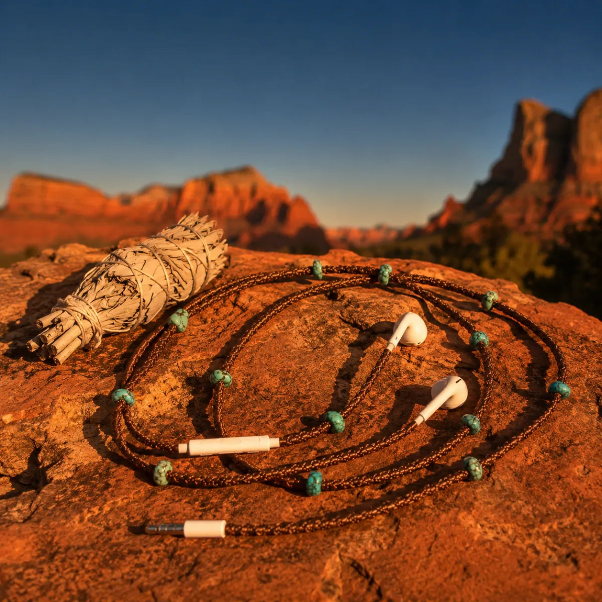  Boho turquoise macrame earphone wrap draped over a red sandstone rock with dried sage smudge stick at golden hour in the high desert 