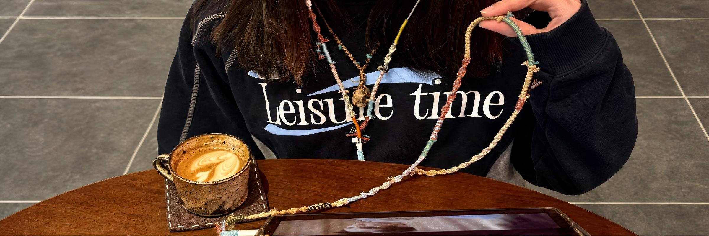 Colorfully wrapped wired earphones worn with a black sweatshirt at a cafe table.